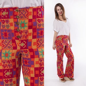 May include: A pair of high-waisted, wide-leg pants with a colorful geometric pattern in shades of red, orange, green, purple, and yellow. The pants have a button fly and a flared leg.