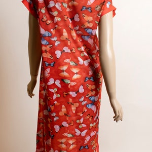 May include: A red, short-sleeved dress with a mandarin collar and a butterfly print. The dress is made of a sheer fabric and has a loose fit.