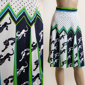 May include: A white, black, and green A-line skirt with a geometric pattern of black panthers and white polka dots. The skirt has a green and blue waistband.