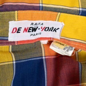 May include: A yellow, orange, red, and blue plaid shirt with a white label that reads "DE NEW-YORK R.A.F.A. PARIS".