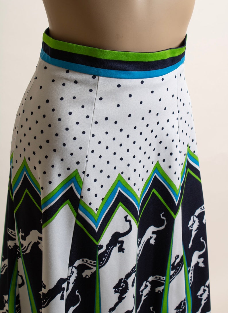 May include: A white skirt with a black polka dot pattern and a green, blue, and black geometric print. The skirt has a wide waistband with a green, blue, and black striped pattern.