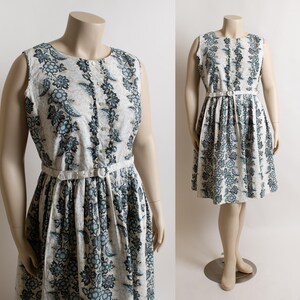 May include: Vintage sleeveless dress with a blue and white floral design. The dress has a button-down front, a fitted waist, and a matching belt. The dress is displayed on a mannequin.