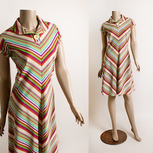 May include: A short-sleeved dress with a colorful striped pattern in shades of red, green, blue, and white. The dress has a V-shaped neckline and a button closure at the collar.