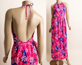 May include: A halter-neck maxi dress in a vibrant pink hue, adorned with a floral pattern in white and blue. The dress features a low back and a flowing skirt, displayed on a mannequin.