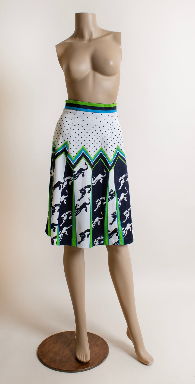 May include: A white skirt with a black and green geometric pattern featuring a repeating design of leaping panthers. The skirt has a white polka dot pattern at the top and a green, blue, and black waistband.