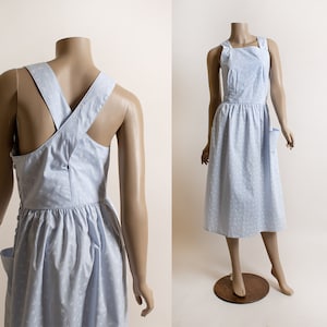 May include: A light blue dress with a white floral pattern. The dress has a criss-cross strap design in the back and a single pocket on the front.