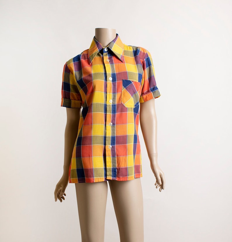 May include: A short-sleeved button-down shirt with a checkered pattern in shades of orange, yellow, blue, and brown. The shirt has a pointed collar and a single chest pocket.