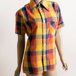 May include: A short-sleeved button-down shirt with a large plaid pattern in shades of yellow, orange, red, and blue.