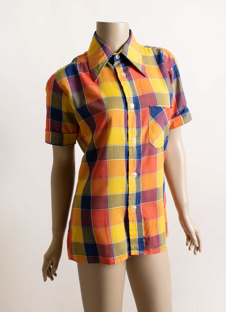 May include: A short-sleeved button-down shirt with a large plaid pattern in shades of yellow, orange, red, and blue.