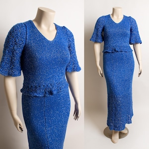 May include: A two-piece blue knit outfit on a mannequin. The top has a V-neck and short, flared sleeves. The skirt is a long, fitted style. The fabric has a subtle sparkle. The outfit is displayed on a mannequin.