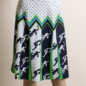 May include: A white skirt with a black polka dot pattern and a green, blue, and black geometric design. The skirt features a repeating pattern of stylized animal figures.
