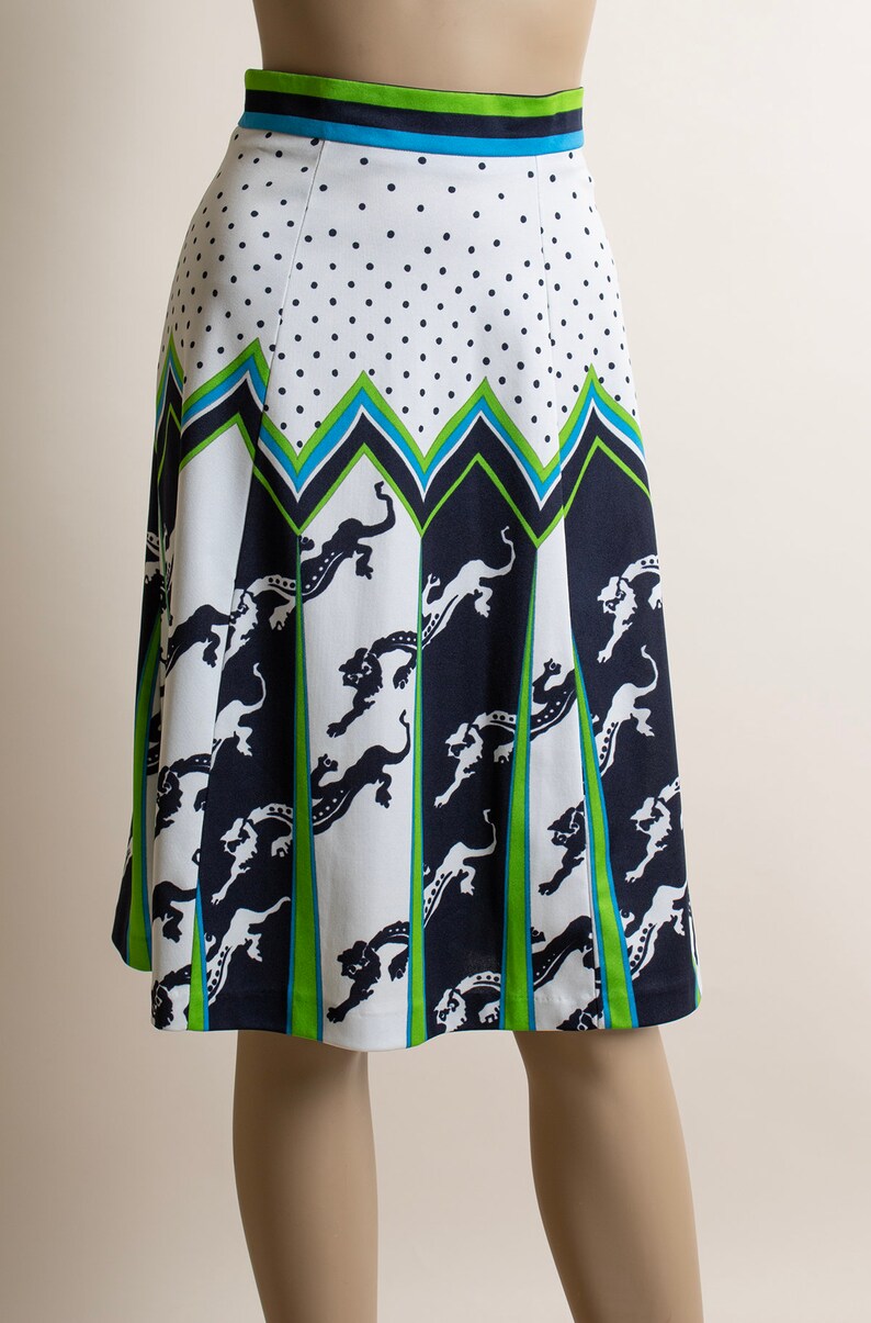 May include: A white skirt with a black polka dot pattern and a green, blue, and black geometric design. The skirt features a repeating pattern of stylized animal figures.