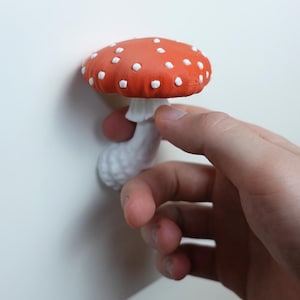 May include: A red and white mushroom with white polka dots. The mushroom has a white stem and is held by a hand. The mushroom is a decorative item.