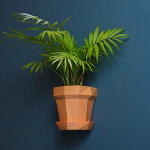 Peut inclure: Un pot de fleurs géométrique pêche avec une soucoupe assortie contient une plante verte vibrante avec de longues feuilles fines. Le pot est monté sur un mur bleu foncé, créant un contraste saisissant. Le design est moderne et minimaliste.