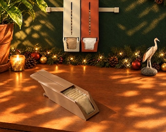Op de afbeelding: Drie rechthoekige theezakjesdispensers, twee verticaal aan een muur gemonteerd en één horizontaal op een oppervlak geplaatst. De dispensers zijn beige en terracotta, voorzien van een verticale gleuf en een open voorvak.