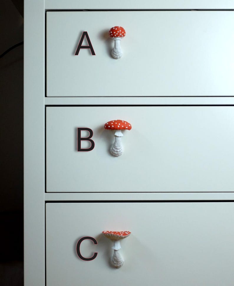 May include: A close-up of a white dresser with three drawers. Each drawer has a dark brown letter and a mushroom-shaped knob. The mushroom knobs have red caps with white spots and white stems. The letters are A, B, and C.
