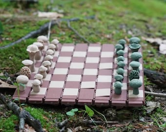 May include: A brown and white checkered chessboard with mushroom-shaped pieces. The pieces are made of a light brown and green material. The board is sitting on a bed of green moss.