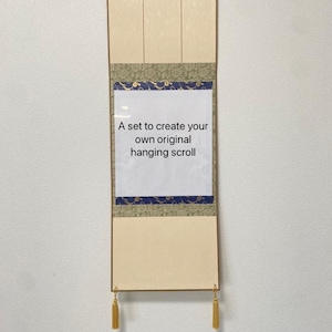 Puede incluir: Un rollo colgante de color crema con un borde decorativo verde y azul. El rollo está en blanco y tiene una etiqueta blanca que dice "Un conjunto para crear tu propio rollo colgante original".