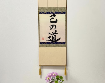 Puede incluir: Un rollo japonés tradicional con caligrafía negra sobre un fondo crema. El rollo está montado en un marco de madera y tiene borlas doradas. La caligrafía dice "El Camino".