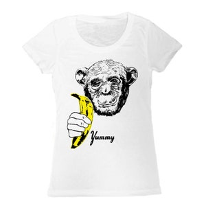 Puede incluir: Camiseta blanca con una ilustración en blanco y negro de un mono sosteniendo un plátano amarillo. El texto "Yummy" está impreso debajo del mono.