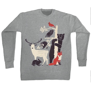 May include: A gray sweatshirt featuring a whimsical forest scene. The design includes a white deer, black bear, red fox, and other woodland creatures. A red cardinal sits atop a tree branch. The sweatshirt has long sleeves and a crew neck.