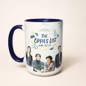 May include: A white ceramic mug with a navy blue handle and interior. The mug features the text "THE OPPA'S LIST" in English and Korean, along with images of four people. Decorative floral elements surround the text.