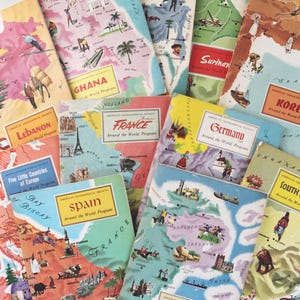 May include: A collection of vintage travel guides from the American Geographical Society's "Around the World Program." The covers feature colorful illustrations of various countries, including Russia, Ghana, France, and Spain. The guides are stacked together.
