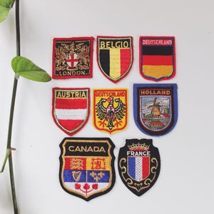 Puede incluir: Una colección de parches bordados con banderas y emblemas de países. Los parches incluyen banderas de Londres, Bélgica, Alemania, Austria, Holanda, Canadá y Francia. Cada parche tiene una forma y diseño únicos, con colores vibrantes y costuras detalladas.