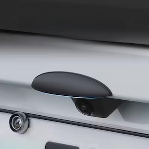May include: A close-up of a car's rear with a black, oval-shaped handle and a backup camera. The handle has a subtle blue light accent. A small, round light is also visible.