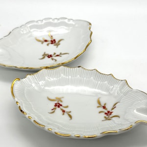 Puede incluir: Dos platos de porcelana blanca en forma de hoja con borde dorado y diseños florales rojos.