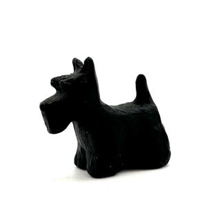 Puede incluir: Pequeña figura negra de un perro Scottish Terrier. El perro está sentado con la cola levantada y las orejas erguidas. La figura tiene una superficie texturizada y está sobre un fondo blanco. Un objeto decorativo encantador para los amantes de los perros.