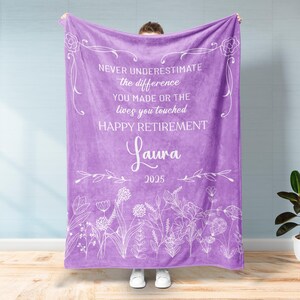 May include: A lavender blanket with white floral and botanical illustrations. The blanket has the text "NEVER UNDERESTIMATE the difference YOU MADE OR THE lives you touched HAPPY RETIREMENT Laura 2025."