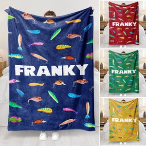 Peut inclure: Une couverture en polaire bleue avec un motif de leurres de pêche colorés et le nom "FRANKY" imprimé en blanc.