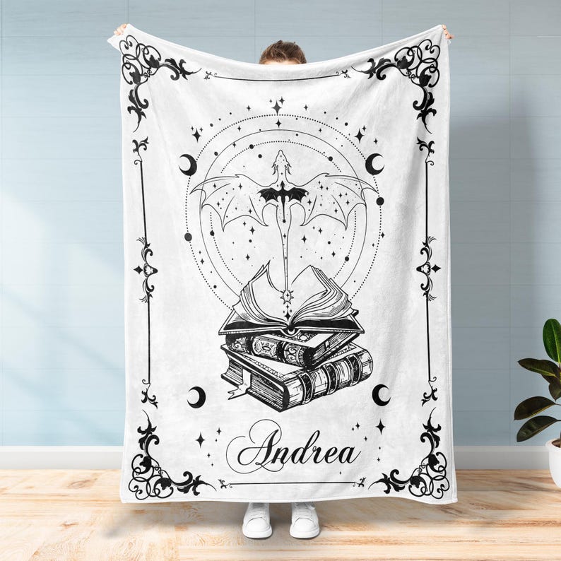 May include: Black and white illustration of a dragon flying over a stack of books with the name Andrea written below. The design is surrounded by a decorative frame and stars.