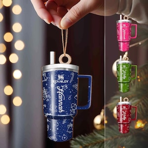 May include: A blue Stanley mug ornament with a handle, featuring a winter holiday design and the name "Hannah" in white script. Additional ornaments in pink, green, and red are also shown, each with a different name.