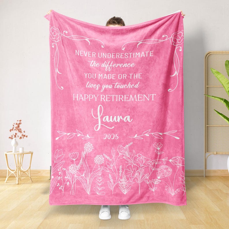 May include: A vibrant pink blanket with white floral accents and text. The text reads "NEVER UNDERESTIMATE the difference YOU MADE OR THE lives you touched HAPPY RETIREMENT Laura 2025". The blanket is a soft, cozy textile.