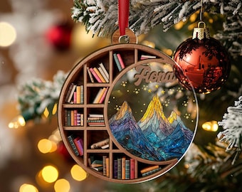 May include: A wooden Christmas ornament with a bookshelf design and a mountain scene. The ornament features the name "Fiona" and is hanging from a red ribbon. A red and gold ornament hangs nearby.