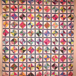 May include: A colorful quilt with a repeating pattern of diamond-shaped blocks. Each block features four smaller triangles in vibrant colors like pink, blue, yellow, and green. The quilt is bordered by a dark blue grid and a light blue edge.