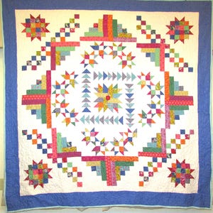 May include: A square patchwork quilt featuring a central star motif surrounded by geometric patterns, including log cabin blocks and small triangles in various colors like pink, green, orange, and blue, all framed by a solid blue border.