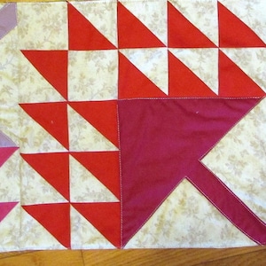 May include: A quilt with a patchwork design featuring pink, red, purple, and gray triangles on a white background with a floral pattern.
