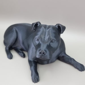 May include: A black 3D printed figurine of a dog lying down. The dog has a short, smooth coat and a short tail. The figurine is detailed and realistic.