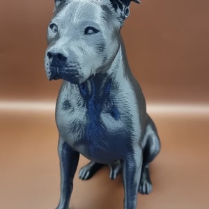 May include: A 3D printed figurine of a black dog sitting with its head tilted slightly to the side. The dog has a short, smooth coat and a defined muzzle.