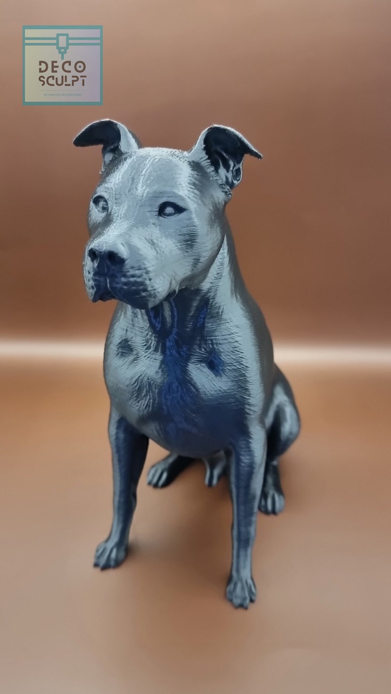 May include: A 3D printed figurine of a black dog sitting with its head tilted slightly to the side. The dog has a short, smooth coat and a defined muzzle.