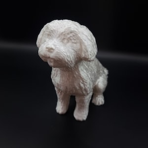 May include: A white 3D printed figurine of a small dog sitting with its head tilted to the side. The dog has a fluffy coat and a sweet expression.