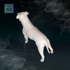 May include: White ceramic sculpture of a dog viewed from above. The dog is standing with its tail curled up. The sculpture is on a dark blue background with a white, swirling pattern.