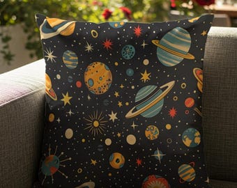 May include: A square throw cushion featuring a dark black background with a repeating pattern of colourful planets, rings, and stars. The celestial design includes various spheres in shades of orange, blue, and yellow, scattered among white dots.