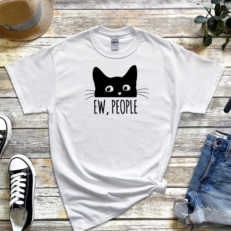 Pu&ograve; includere: Maglietta bianca con un gatto nero che spunta da sopra e il testo "EW, PEOPLE".