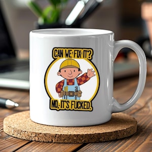 Puede incluir: Taza de cerámica blanca con un dibujo animado de un trabajador de la construcción y el texto "CAN WE FIX IT?" y "NO, IT'S FUCKED!". La taza está sobre un posavasos marrón. La taza tiene un asa.
