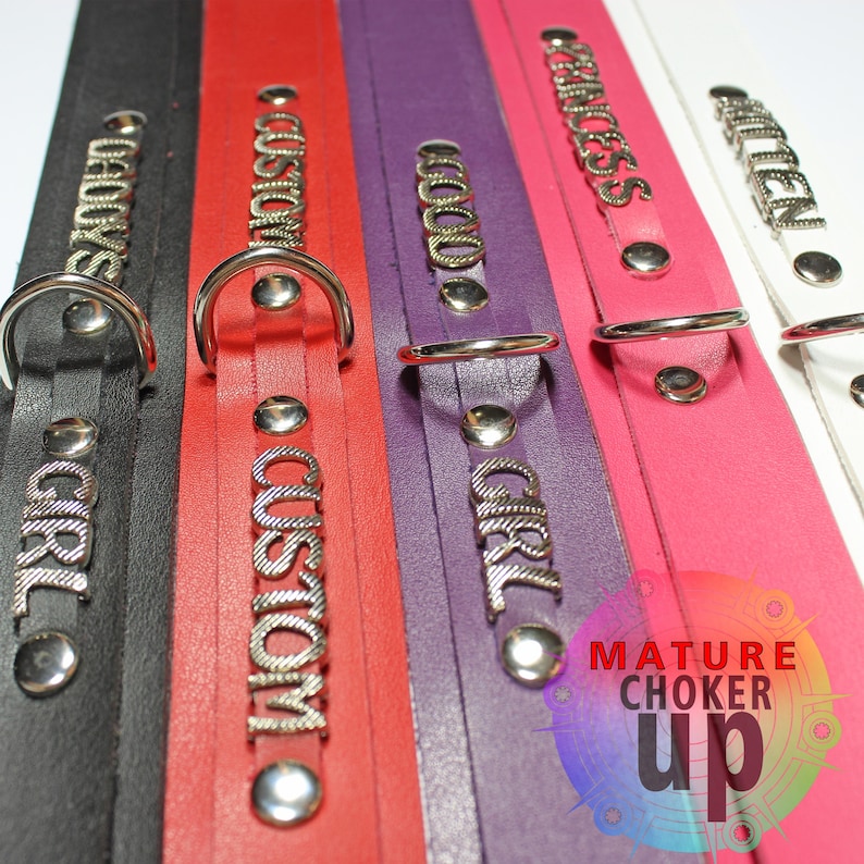 May include: Five leather chokers with metal rings and studs. The chokers are black, red, purple, pink, and white. Each choker has a different word embossed on it: "Bad Girl", "Custom", "Good Girl", "Princess", and "Milen".