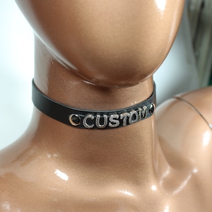 May include: A black leather choker with silver metal lettering that reads "CUSTOM".